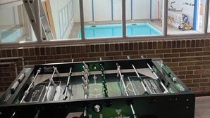 Une table de baby-foot ornée du logo « Carlsberg », un mur de briques et une vue sur une piscine, visible à travers de grandes fenêtres.