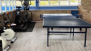 Une salle de sport équipée de matériel d’exercice, d’une table de ping-pong et dotée de grandes fenêtres.