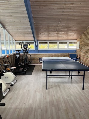 A gym with exercise equipment, a ping pong table, and large windows.