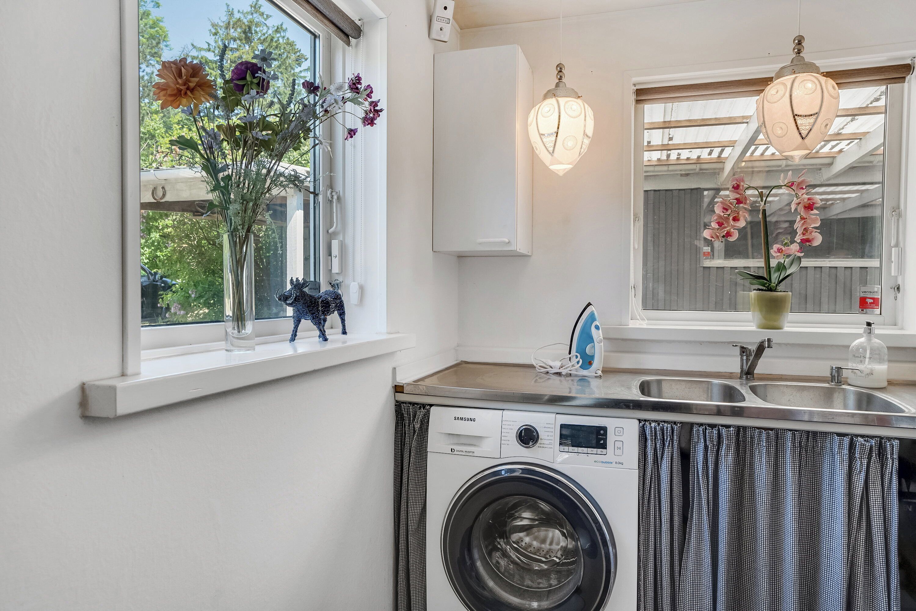 A laundry area with a washing machine, a sink, and a window with flowers.