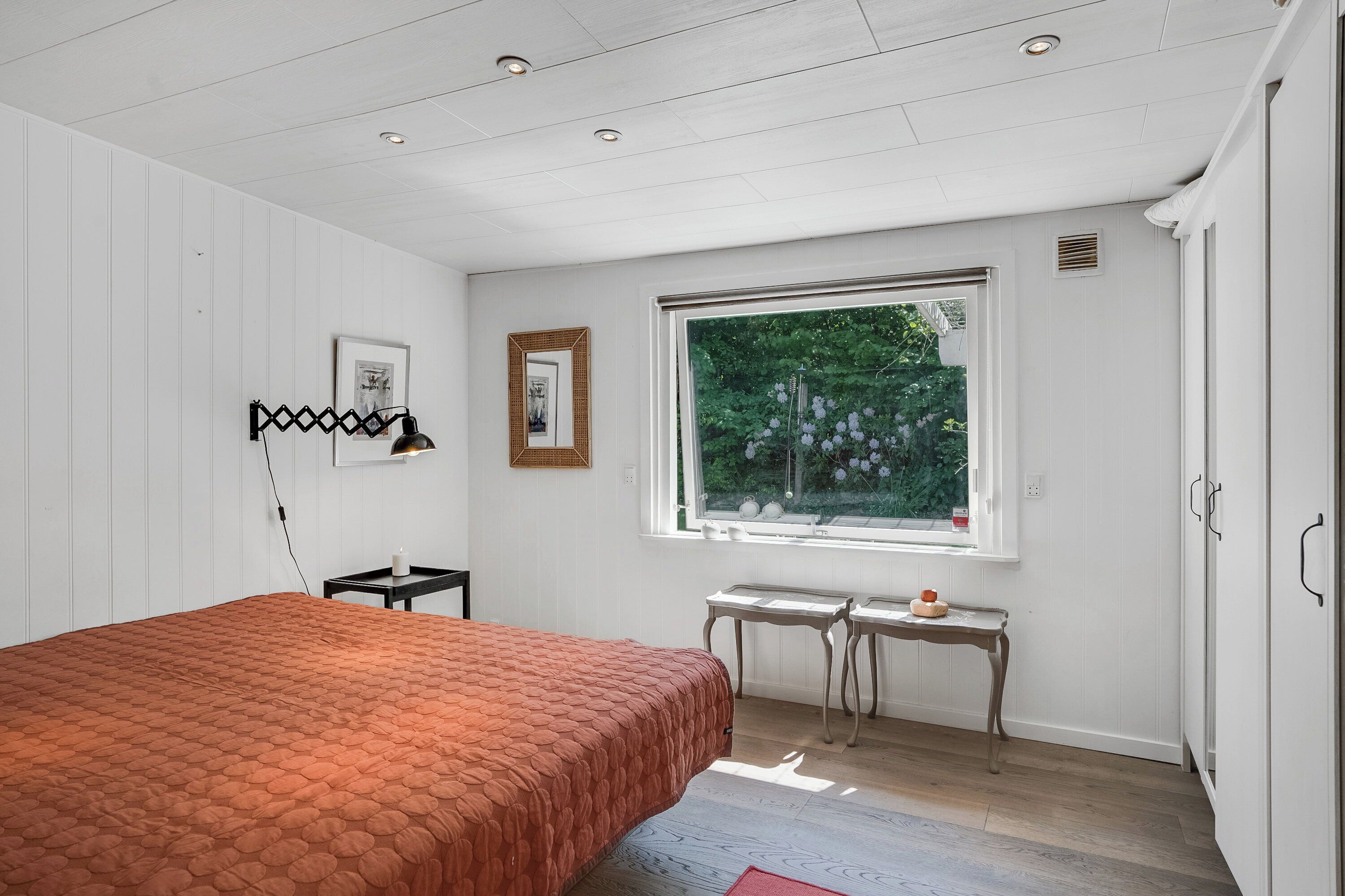 Ein Schlafzimmer mit Bett, Fenster mit Blick, Nachttisch und Wandlampe.
