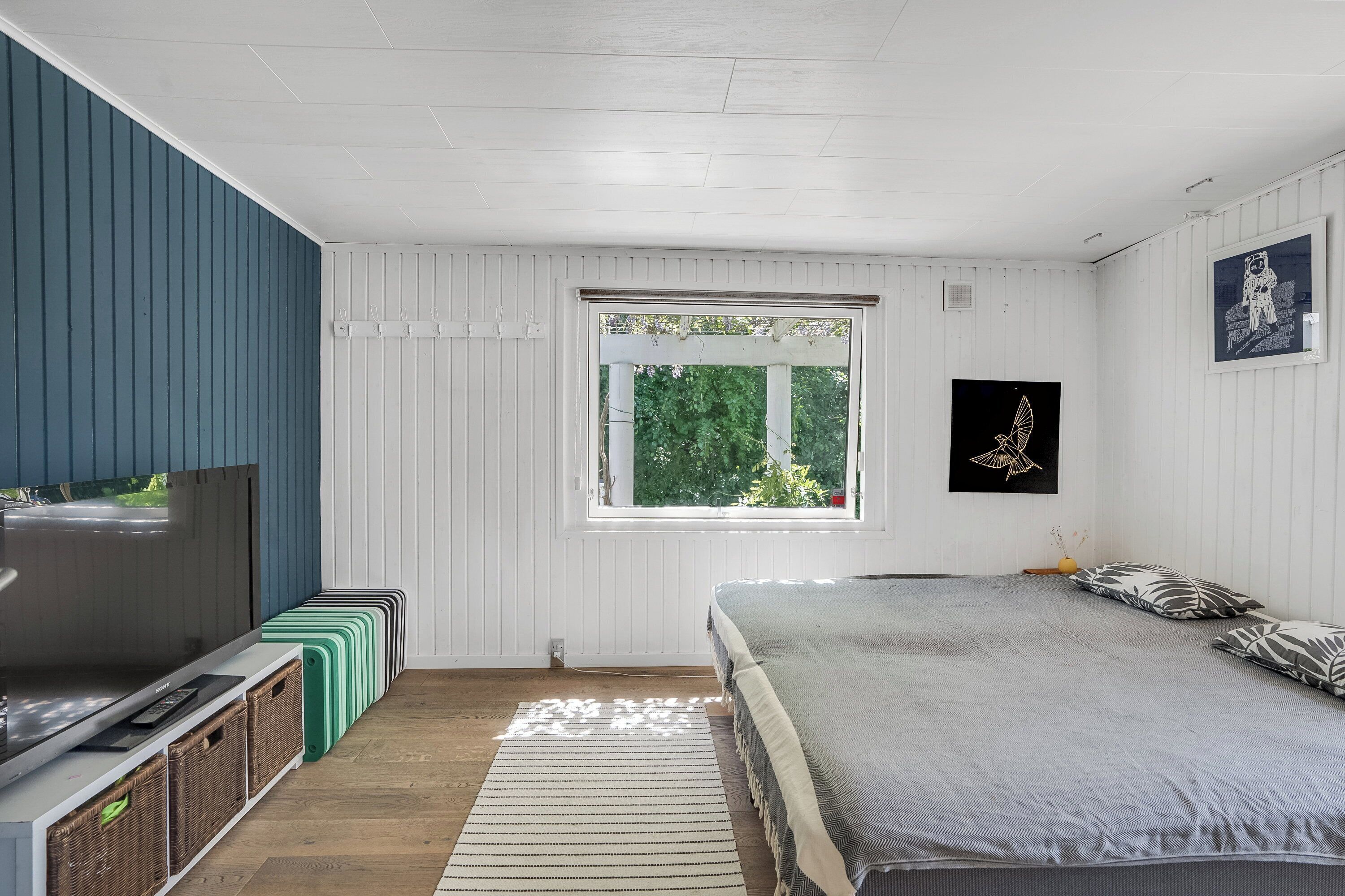 Une chambre avec un lit, une télévision, une fenêtre et un mur orné d’un tableau.