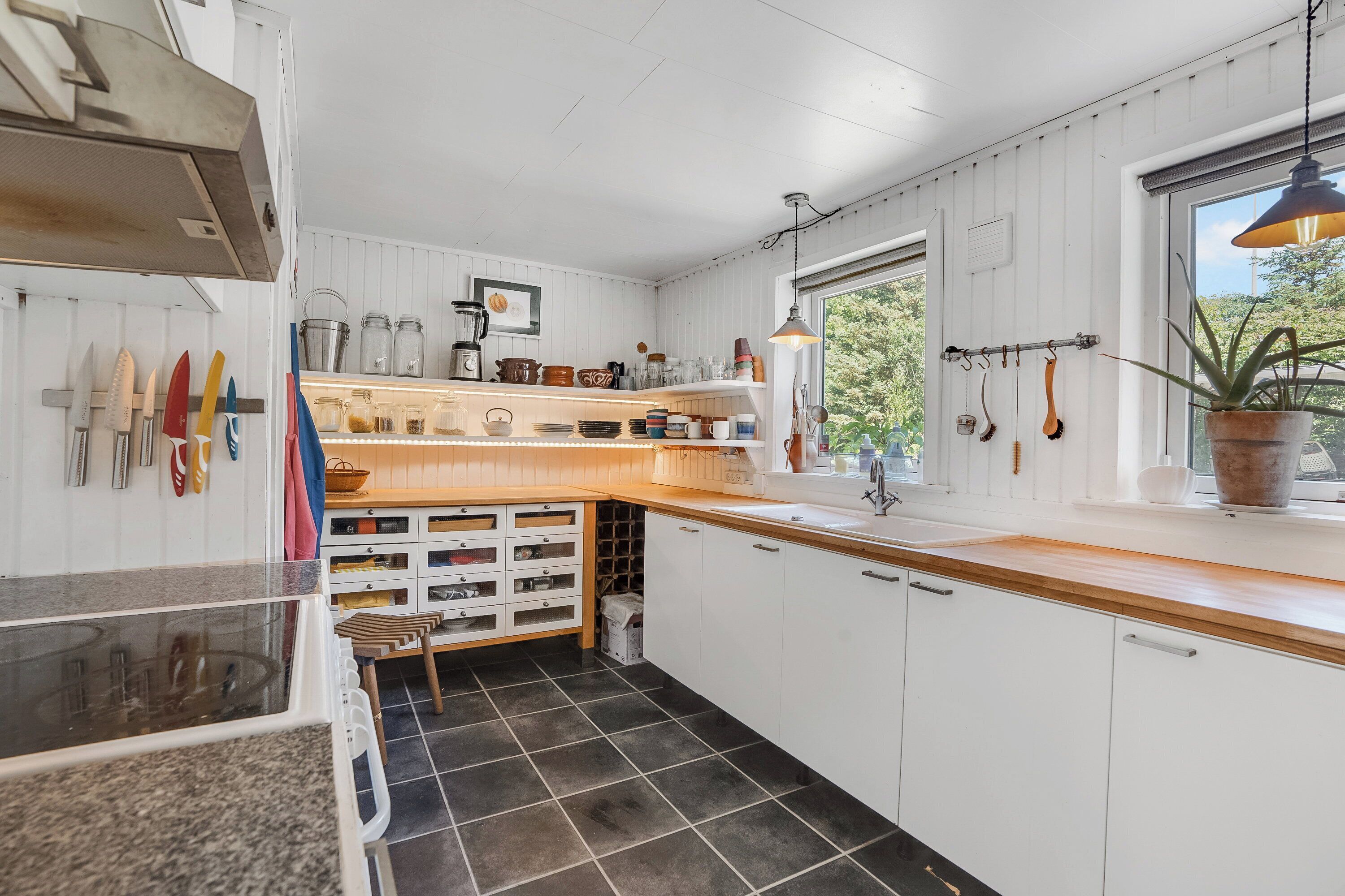 A kitchen with white cabinets, a wooden countertop, and a window with a view of greenery.