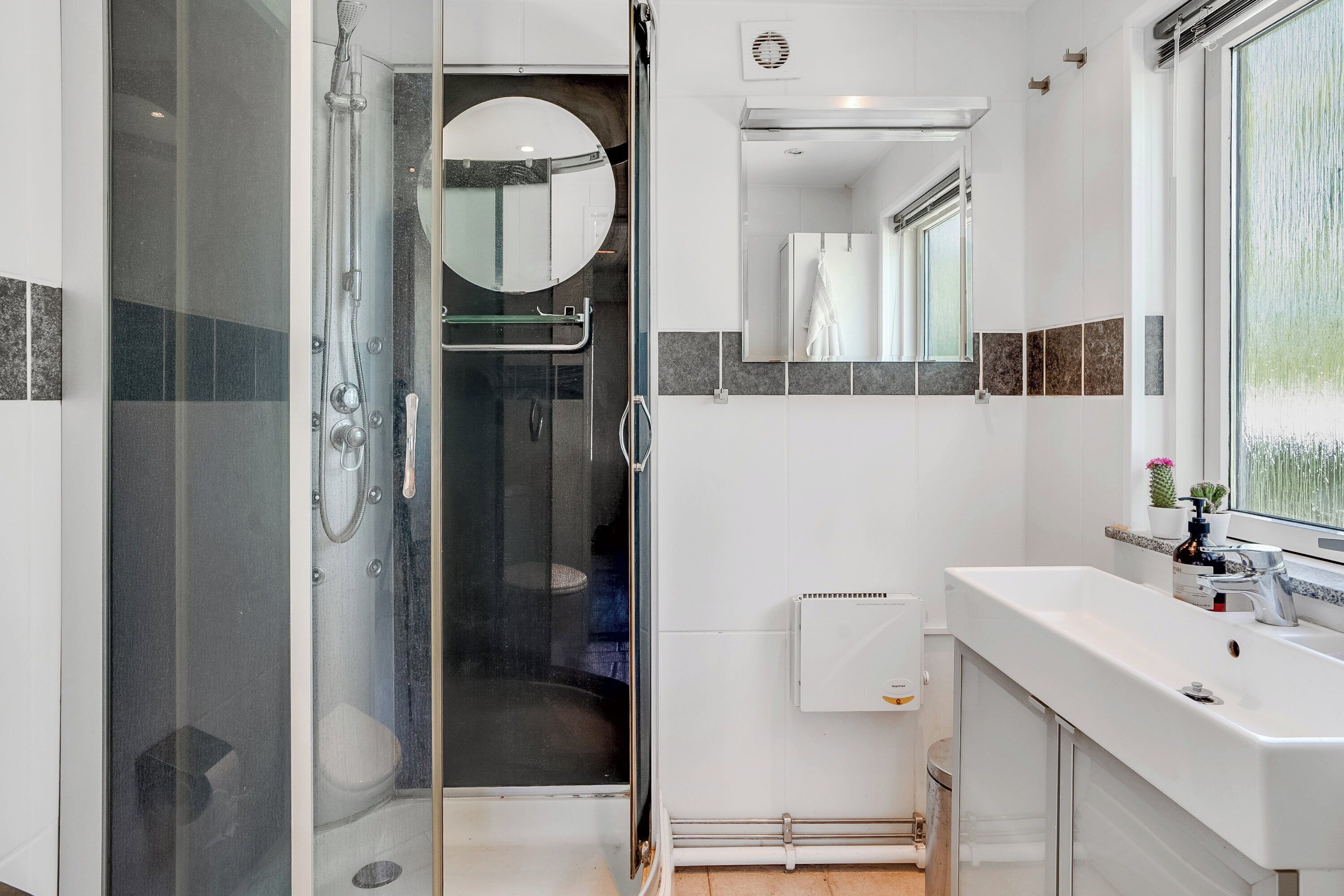 Une salle de bain moderne avec une douche à parois de verre, un miroir rond, un lavabo blanc et une fenêtre donnant sur un beau paysage.