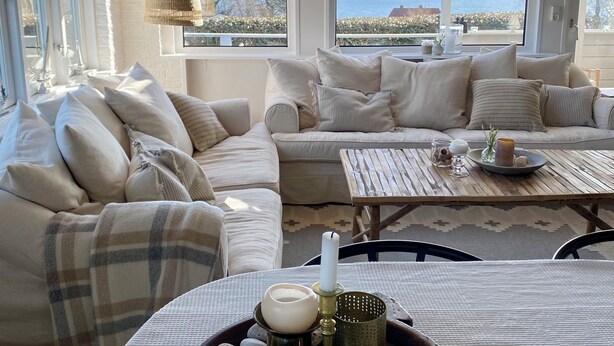 A cozy seating area with a sofa and chairs, a table with decorative items, and large windows offering a view of the sea. - Stunning home in Unknown with 3 Bedrooms and WiFi (Allinge)