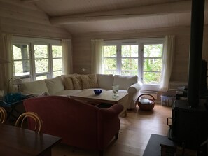 Une pièce chaleureuse avec un plafond en bois, un canapé, un fauteuil rouge, une table et une cheminée.