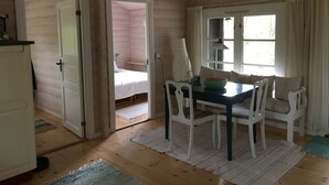 A wooden cabin interior with a dining table, chairs, a bed, and a window with curtains. - Log house near a child-friendly sandy beach (Nykøbing Sjælland)