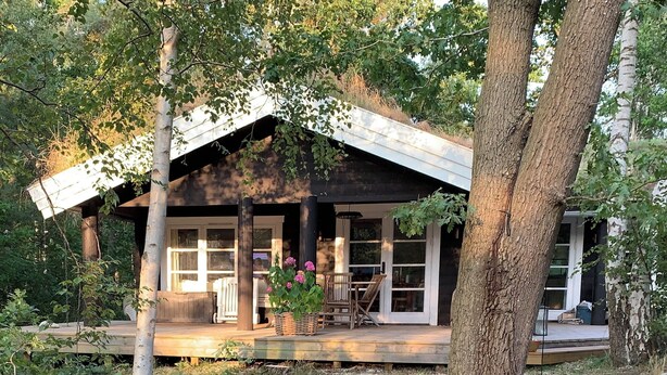 A wooden cabin with a porch, large windows, and a garden with flowers. - Log house near a child-friendly sandy beach (Nykøbing Sjælland)