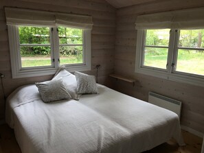 A bedroom with a bed, two windows with curtains, a bedside table, and a radiator.