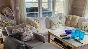 A cozy living room with a grey sofa, a wooden coffee table, and a window with curtains. - Log house near a child-friendly sandy beach (Nykøbing Sjælland)