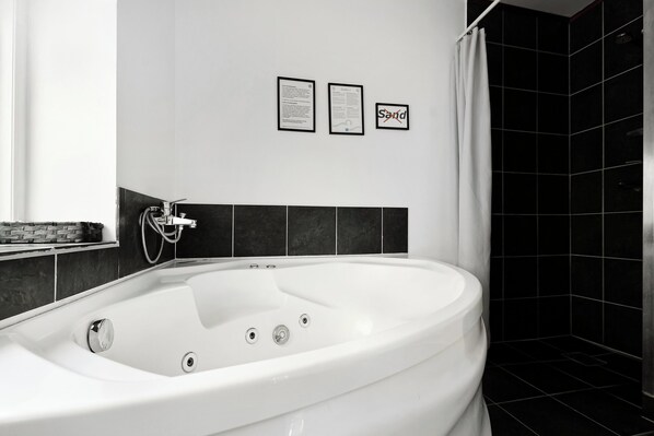 Un baño moderno con una bañera blanca, paredes cubiertas de baldosas negras y carteles informativos enmarcados.