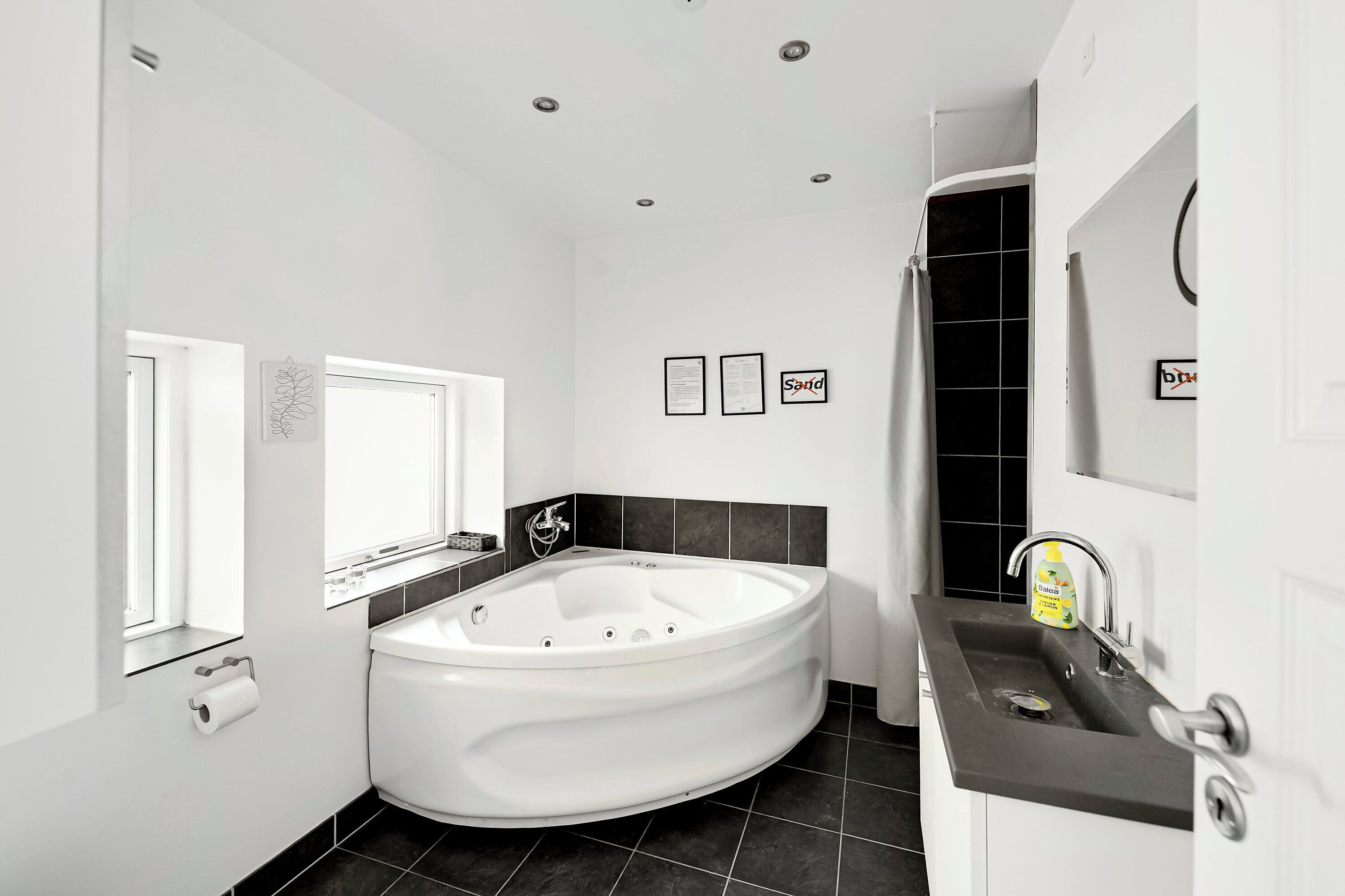 A modern bathroom with a freestanding bathtub, a sink with a soap dispenser, and a window.