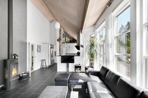 Una sala de estar moderna con chimenea, sofá de cuero negro y ventanas amplias.