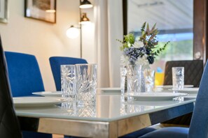 Un tavolo da pranzo apparecchiato con bicchieri trasparenti, sedie blu e un vaso con fiori.