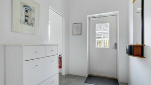 En hall med en vit dörr, en brandsläckare, en inramad tavla på väggen och en liten hylla med en spegel.