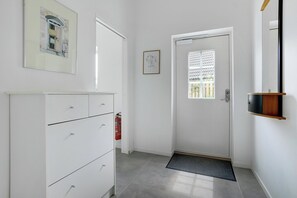 Ein Flur mit einer weißen Tür, einem Feuerlöscher, einem gerahmten Bild und einem kleinen Regal.