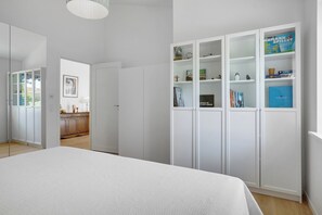 A bedroom with a large bed, white wardrobe, and a view to the dining area. - New and cozy house by the beach and forest (Hornbæk)