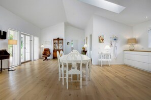 Een ruime kamer met een eettafel, stoelen, een piano en een groot raam.