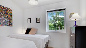 Ett sovrum med två sängar, ett fönster med utsikt över grönområden, en byrå och en färgstark, abstrakt målning på väggen.
