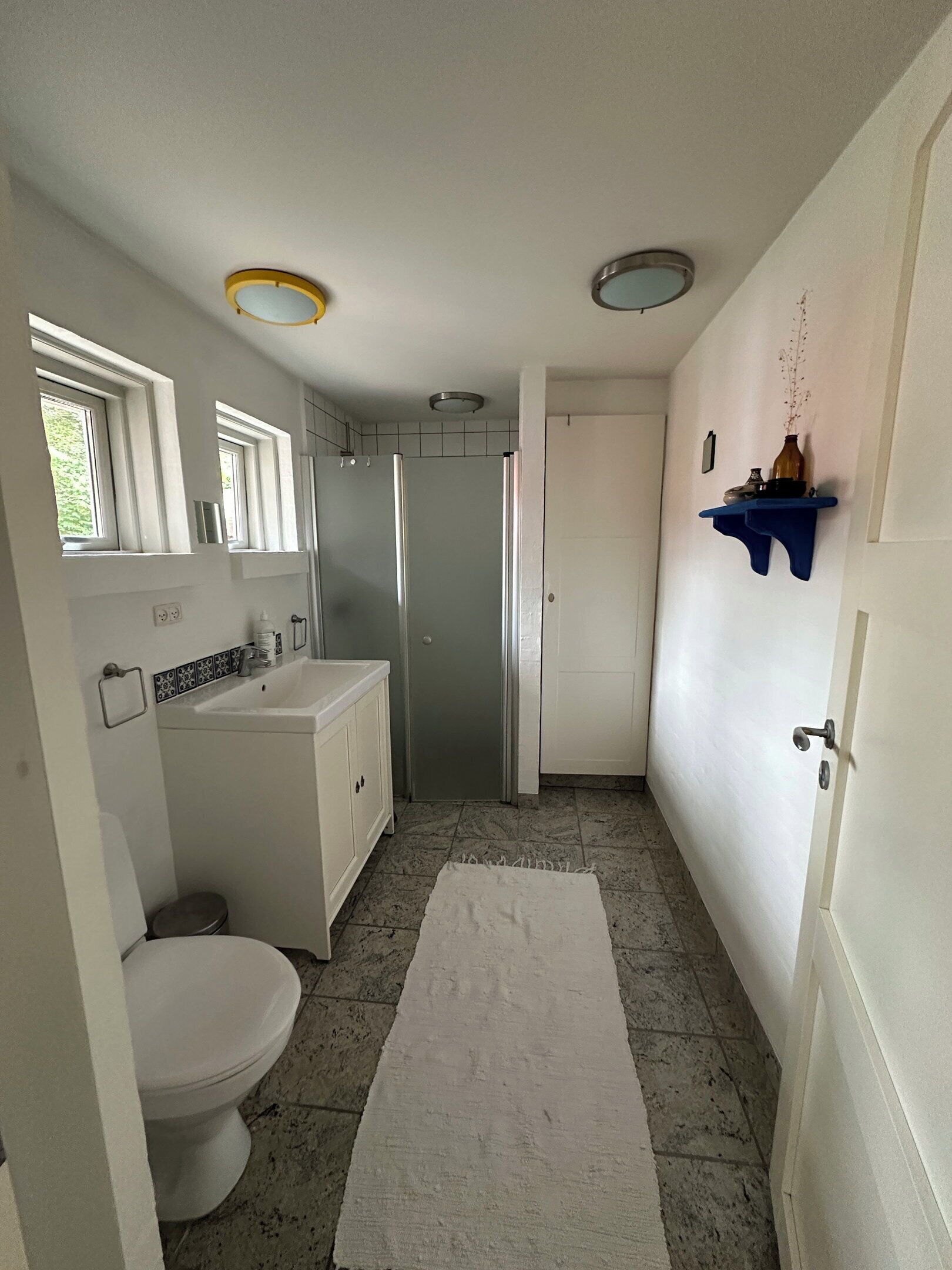 A bathroom with a toilet, sink, shower, and a white rug on the floor.