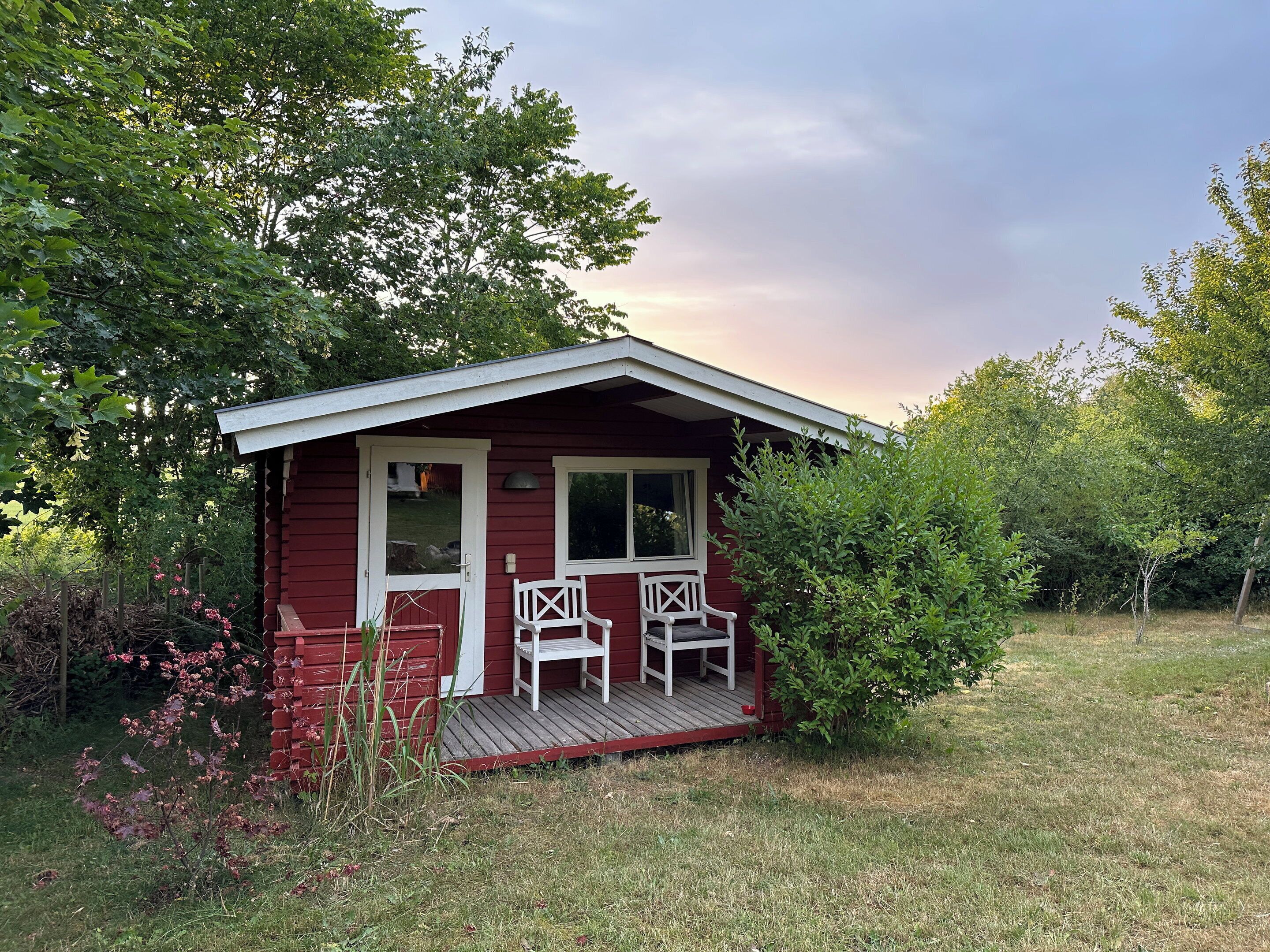 A small red cabin with a porch and two white chairs.