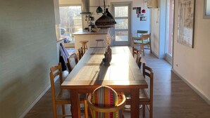 Uma sala de jantar com uma mesa e cadeiras de madeira, uma cozinha ao fundo e uma porta que dá para o exterior.