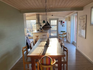 Ein Essbereich mit Holztisch und -stühlen, im Hintergrund eine Küche und eine Tür zum Außenbereich.
