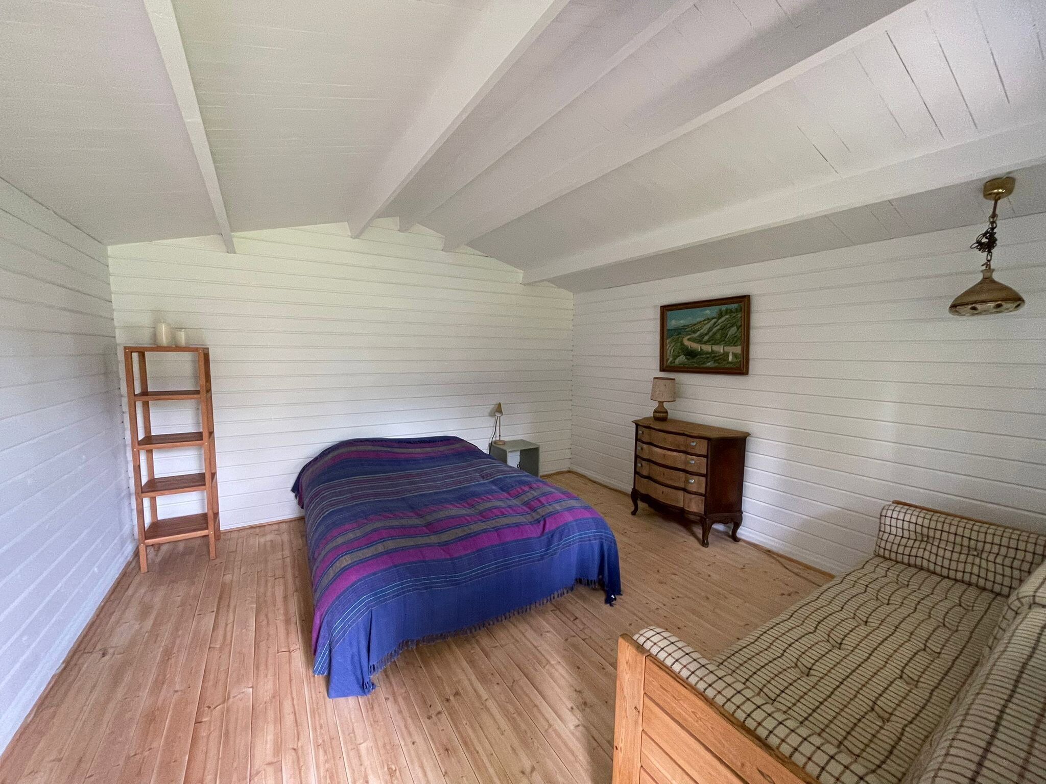 Ein Schlafzimmer mit einem Bett, einem Schminktisch, einem Nachttisch, einer Leiter und einem Bild an der Wand.