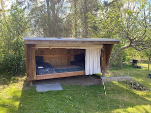 A small wooden cabin with a single bed, a bench, and a covered seating area. - Family friendly holiday home in Orø (Holbæk)