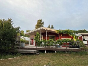 A red wooden house with a covered porch, a small garden, and a greenhouse. - Family friendly holiday home in Orø (Holbæk)