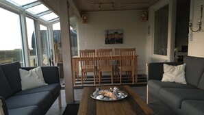 Una sala de estar moderna con techo de vidrio, dos sofás, una mesa de centro de madera y una mesa de comedor con sillas.