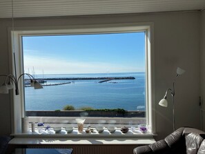 A room with a large window overlooking a calm sea, a chair, and a table with various items. - Spacious house with sea views from all rooms (Rønne)