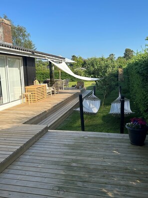 A wooden deck with outdoor furniture, a pergola, and hanging chairs.