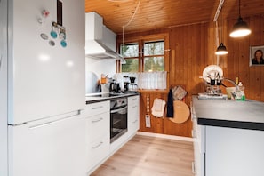 Une cuisine avec des murs en bois, un rĂ©frigĂ©rateur blanc, une cuisiniĂšre et une fenĂȘtre ornĂ©e de rideaux en dentelle.