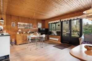 Ein Zimmer mit Holzwänden, einem Esstisch, Stühlen, einer Küchenzeile und großen Fenstern.