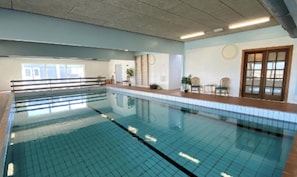 An indoor swimming pool with clear water, tiled walls, and a ceiling with visible beams.