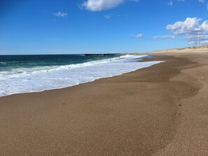 Ein Strand mit klarem Himmel, Wellen und einer fernen Felsformation.