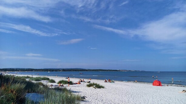 En strand med sand, vand og en blå himmel.
