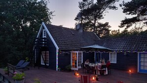 En træterrasse med udendørs møbler, en overdækket terrasse og et hus med mørkt tag og hvide detaljer.