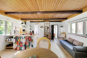 A cozy interior with a wooden ceiling, a dining area with a table, a sofa, and a ladder leading to a loft.