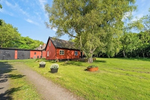 A red building with a sloped roof, surrounded by a grassy area and trees. - Cozy and original holiday home on Bornholm (Nexø)