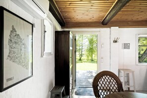 A room with a wooden ceiling, a door leading outside, a framed picture on the wall, and a small table with a chair.