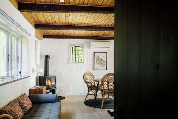 A cozy room with a wooden ceiling, a sofa, a table with chairs, a fireplace, and a window.