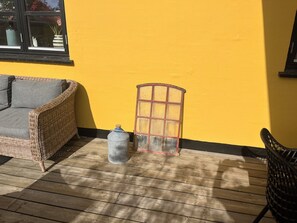 A wicker sofa, a metal container, and a glass cabinet on a wooden deck against a yellow wall. - Lovely spacious holiday home on Bornholm (Hasle)