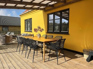 Una terraza de madera con una mesa y sillas, una pared amarilla y una ventana.