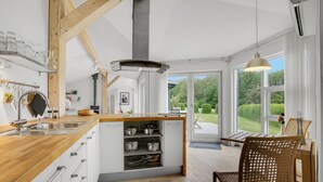 A modern kitchen with wooden beams, a built-in island with storage, a large window, and a view of greenery.