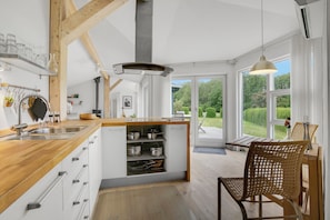 Una cocina moderna con vigas de madera, una isla integrada con espacio de almacenamiento, un ventanal y vistas al verdor.