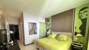 A hotel room with a bed, a nightstand, a lamp, a mirror, and a painting on the wall. - Charming bedroom in luxurious villa with seaview (EZE)