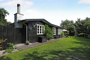 Ein schwarzes Holzhaus mit Schornstein, einem umzäunten Garten und einem gepflegten Rasen.