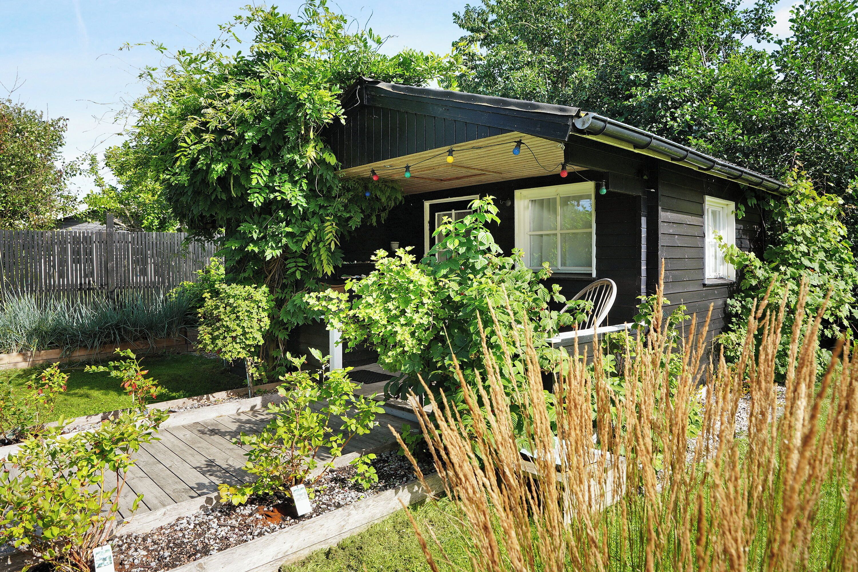 Ein kleines Haus mit einer Veranda, umgeben von einem Garten und einem Holzzaun.